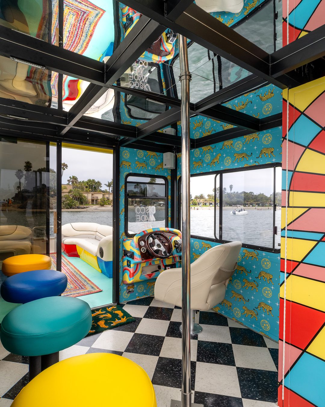 Disco Boat interior — rainbow bar stools, sunburst-and-disco-ball door, San Diego Bay through the windows