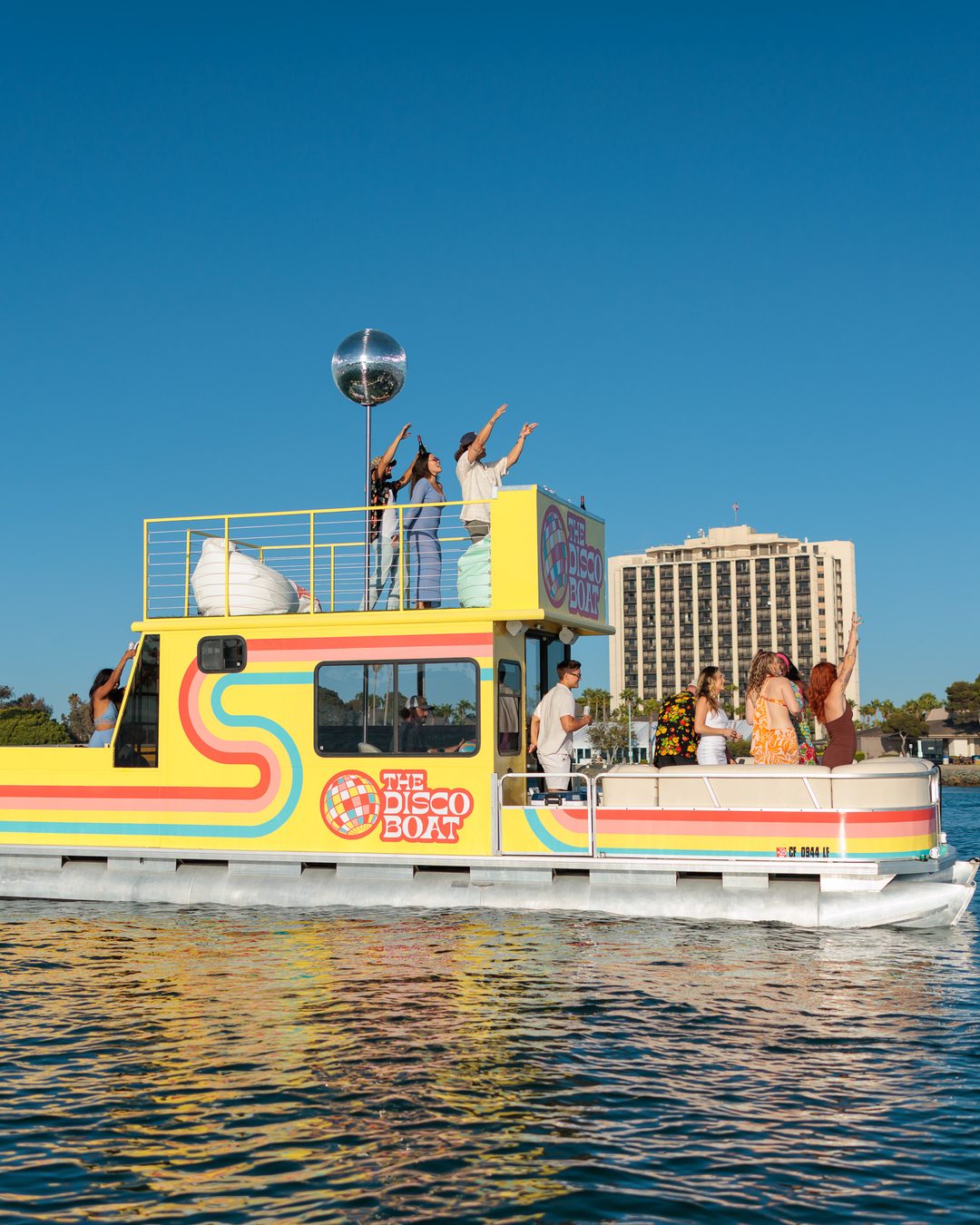 Themed cruise on the Disco Boat — guests on the rooftop with arms raised under the mirrored disco ball